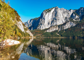 Fototapeta na wymiar Altaussee, Styria, Austria - A view over Lake Altaussee to the Trisselwand, part of the Totes Gebirge, on a sunny cloudless day in golden October with blue skies.