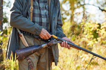 Fototapeta premium Man holding shotgun loading it. Forest background. Hunting, people concept