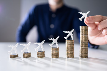 Human Hand Placing Small Airplane On Increasing Stacked Coins
