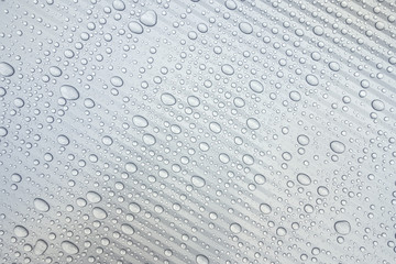 Wassertropfen auf einer hellgrauen Kunststoffoberfläche mit leichtem diagonalen Streifenmuster