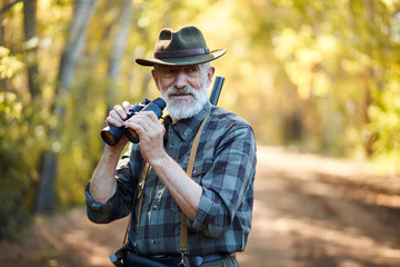 Using binoculars for better hunting on birds. Senior man holding binoculars during hunting in...