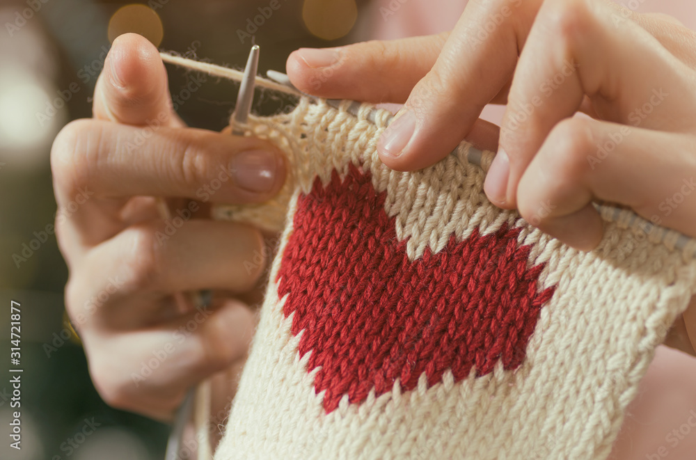 Wall mural Concept of love and concern. Woman knitting the red heart for her loved one. Valentines postcard.