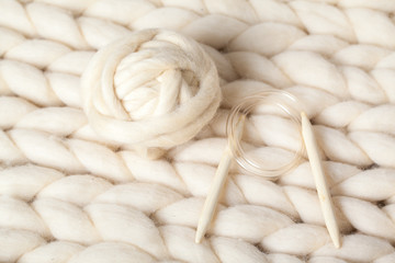 a ball of thick yarn and wooden needles lie on a blanket of Merino wool