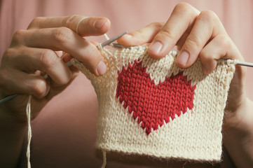 Concept of love and concern. Woman knitting the red heart for her loved one. Valentines postcard.