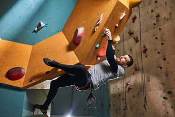 Fototapeta na wymiar Flexible young physically challenged boulderer overhanging at large rock wall, rising up quickly, strong-willed and motivated person, overcomes life troubles and difficulties, inspiration concept.