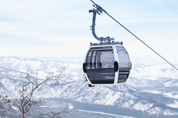 Cabin of a gondola cableway suspended on a rope where sits people with skis and snowboards high in...