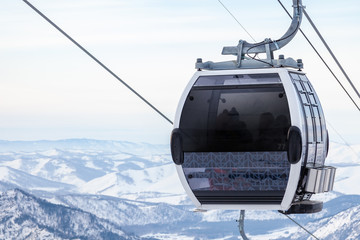 Cabin of a gondola cableway suspended on a rope where sits people with skis and snowboards high in...