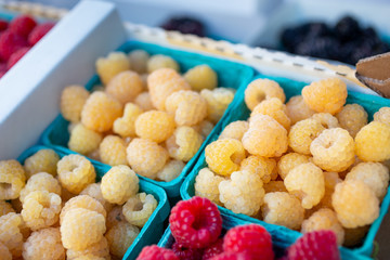 A closeup look of several containers full of white raspberries next to some red raspberries on display at a local farmers market.