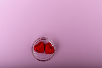 Red heart shaped sweets in glass plate are on a pink blue background. Greeting card Happy Valentines Day. Copy space.