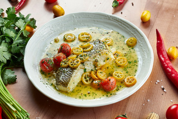 Close up on gourmet Grilled fillet of pike perch on with yellow sauce and vegetables in white bowl on wooden background in composition with ingridients. Healthy food. Restaurant food.