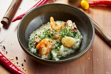 Close up view on Grilled tiger prawns and scallops with risotto in a black bowl on a wooden background. Seafood rice,