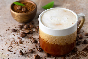 Morning coffee concept. Cup of coffee latte, coffee beans and ground powder on a stone old concrete countertop.