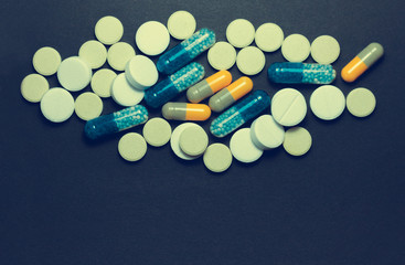 Heap of colorful pills, pharmaceutical medicine tablets and capsules over black background.