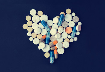 Heap of colorful pills in the shape of a heart, tablets and capsules over black background
