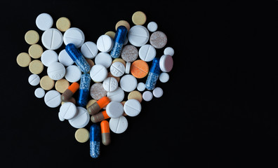Heap of colorful pills in the shape of a heart, tablets and capsules over black background
