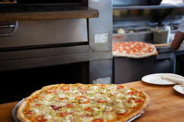 A view inside a pizza restaurant kitchen featuring several pizza pies being made.