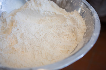 Looking into a steel metal bowl full of flour in a restaurant kitchen setting.