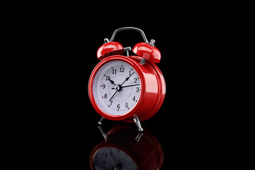 Red alarm clock with reflection on glass close-up isolated on dark background.
