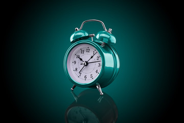 Turquoise alarm clock with reflection on glass close-up isolated on dark background with turquoise gradient.