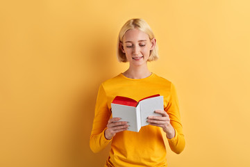 cheerful beautiful woman enjoying reading book, lifestyle, interest, free time, spare time, isolaated yellow background, studio shot