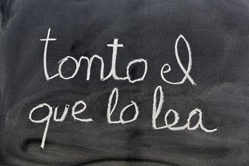 La frase, tonto el que lo lea, escrito con tiza en una pizarra, en el idioma español