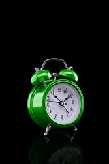 Green alarm clock with reflection on glass close-up isolated on dark background.