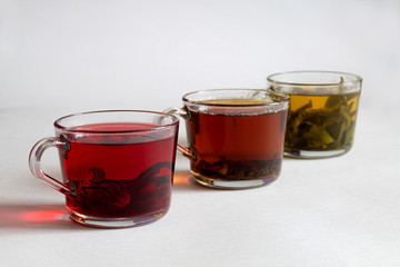 Healthy lifestyle. Hot drinks. Three glass cups with black, red and green tea on a white background. Red hot Hibiscus tea. Green hot tea. Black hot tea.