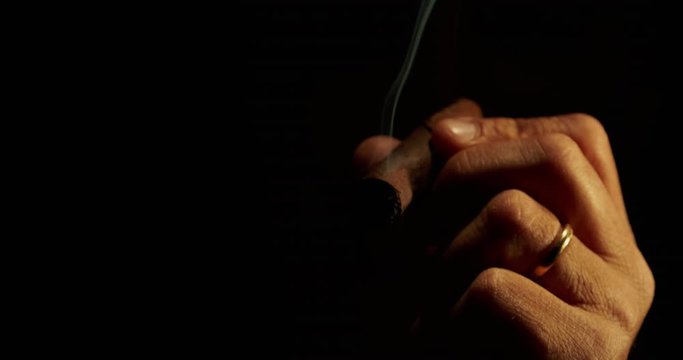 Successful man smoking a cigar in dark background in 4K