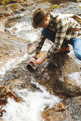 young man in checked shirt. jeans getting water from the stream, close up cropped photo.