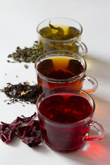 Three glass cups with black, red and green tea on a white background. Red hot Hibiscus tea with dry flowers. Healthy lifestyle.  Green hot tea. Black hot tea. Hot drinks.Vertical orientation.top view