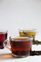 Black hot tea with dry leaves.Three glass cups with black, red and green tea with dry leaves on a white background. Red hot Hibiscus tea. Healthy lifestyle.Green hot tea.Hot drinks.vertical orietation