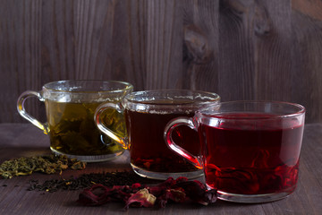 Healthy lifestyle.Hot drinks.Three glass cups with black, red and green tea with dry leaves and...
