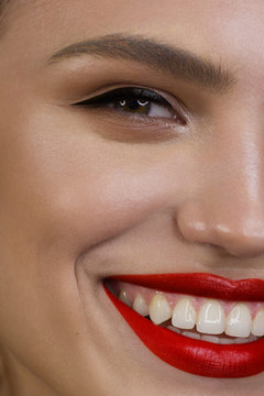 Half Closeup Portrait Of The Cleanliness Of The Face Of A Beautiful Woman With Eyeliner, Red Puffy Lips. A Sexy Model With Clean Skin, Thick Eyebrows And Very Long Eyelashes. Smile With White Teeth