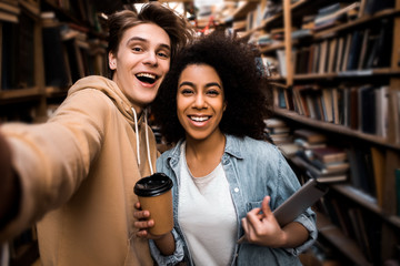 Positive happy selfie photo of two students friends multicultural couple in the library, happy...