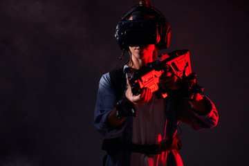 Young girl killer using technology as vr headset, goggles, weapons playing shooter game. Isolated smoky background, neon light