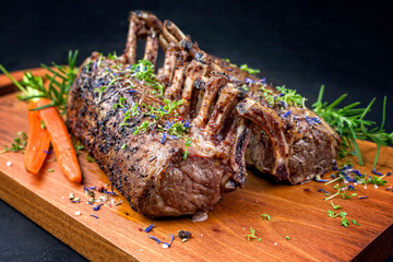 Gegrilltes Lamm Karree mit Karotten und Kräuter angeboten als closeup auf einem Modern Design Holz...