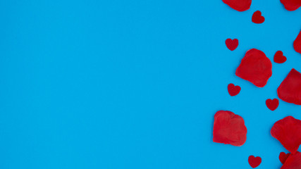 Red rose petals and red hearts lying on a blue background.