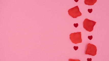 Small red hearts and red rose petals lying on a pink background.