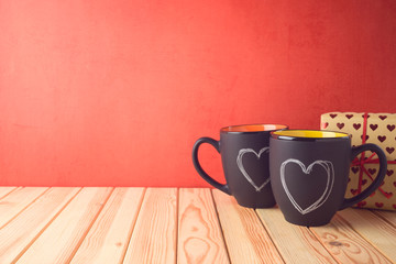 Valentines day concept with chalkboard coffee mugs, heart shapes and gift box on wooden table.