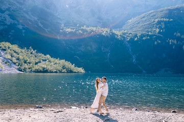 the guy hugs the girl and she bend back on the shore of lake. mo
