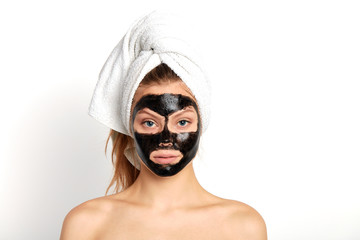 portrait of awesome girl woman in a towel on the head with black nourishing mask on face on white background isolated. Skincare, cleansing, spa concept.studio shot