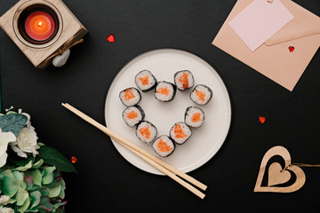Sushi for Valentines Day - roll in heart shape, on plate on black background. Flat lay.