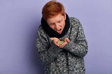 funny guy pretending that he is taking all pills lying on his plams. close up portrait, isolated blue background, studio shot