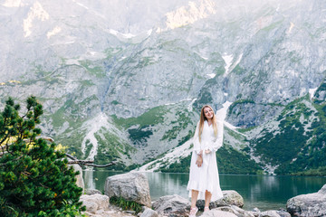 Young woman on shore of mountain lake in white dress. look at ca