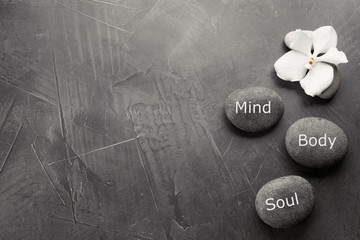 Stones with words MIND, BODY, SOUL on grey background, top view with space for text. Zen lifestyle