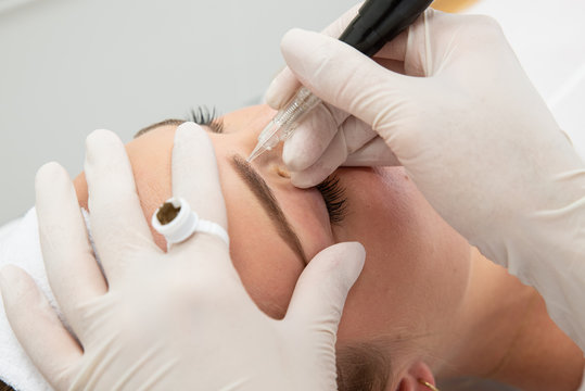 Zbliżenie na proces pigmentacji brwi. Kosmetyczka wykonuje makijaż permanentny brwi. Brwi podczas zabiegu makijażu permanentnego w salonie urody. Zabieg w salonie medycyny estetycznej. Salon urody. 
