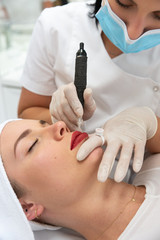 Linergistka wykonuje makijaż permanentny ust. Usta po makijażu permanentnym w salonie kosmetycznym. Mikropigmentacja ust zabieg w klinice medycyny estetycznej. 