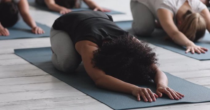 African woman performing Child pose with associates during yoga class