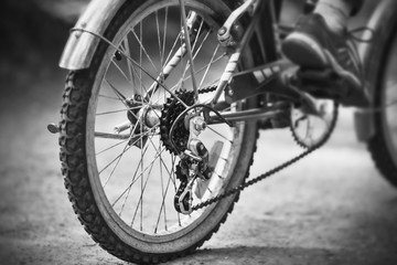 A black-and-white image of the rear wheel of a high-speed sports bike, on which a man in sports shoes is riding fast on a park road.