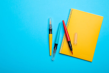 Yellow notebook and markers on light blue background, flat lay. Space for text